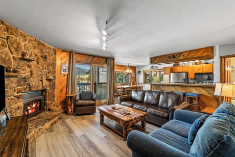 Unwind in your spacious living area with rustic stone fireplace and handcrafted furnishings. The open layout connects you to mountain views through the balcony door and a welcoming kitchen perfect for cozy gatherings.