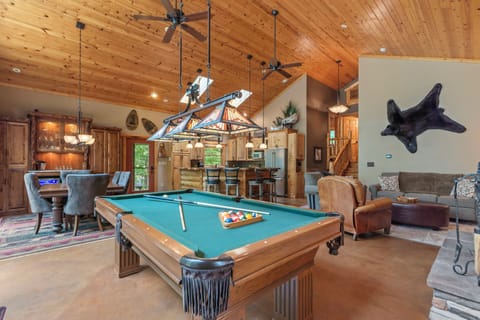 Step into your spacious game room with soaring ceilings and warm wood beams overhead. Challenge friends to pool under charming pendant lighting while cozy seating invites you to unwind after your match.