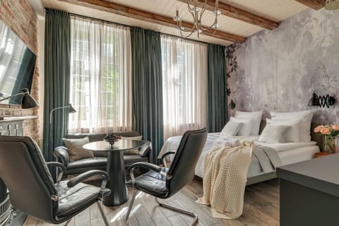 Przestrzeń apartamentu łączy funkcję sypialni i części wypoczynkowej. Znajduje się w niej wygodne łóżko małżeńskie z hotelową pościelą i kompletem poduszek, sofa, fotele ze stolikiem oraz telewizor Smart TV z dostępem do kanałów kablowych.