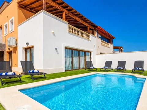 Modern villa backyard featuring a bright blue swimming pool, a manicured green lawn, and multiple black lounge chairs.
