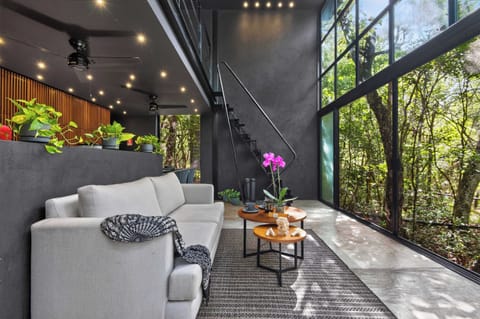 Golden hour pours through the panoramic glass wall — the living room as a meditation in light and jungle