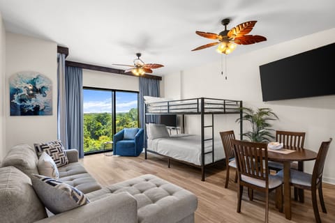 Your open-concept retreat blends comfort and style, featuring a cozy bunk bed, plush seating, and tropical ceiling fans that frame stunning treetop views through expansive windows.