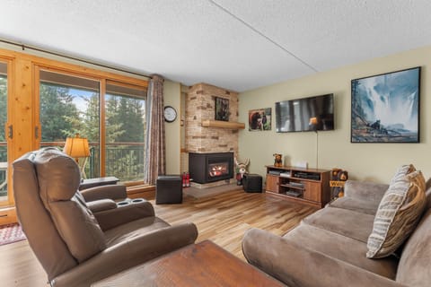 Unwind in your spacious living room with plush seating, a cozy fireplace, and large windows overlooking serene treetops—perfect for relaxing evenings together.