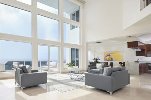 Sink into modern comfort in your light-filled living space, where floor-to-ceiling windows frame stunning ocean vistas and sleek furnishings invite you to unwind in coastal elegance.