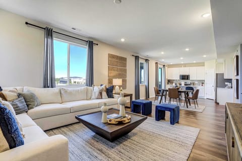 This open concept living room features a plush sectional, wood coffee table, and media console, all flowing into the dining area beyond. Hardwood style flooring and natural light tie the space together.