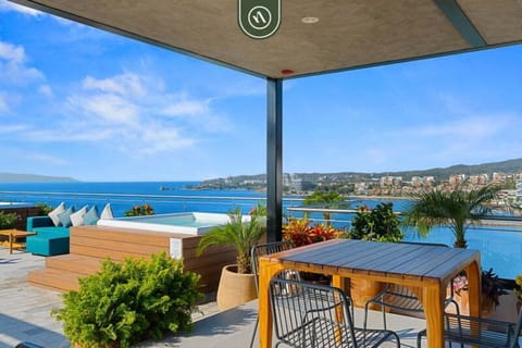 This spectacular rooftop terrace features an elevated wood-paneled hot tub, comfortable outdoor sectional seating, and dining areas overlooking the turquoise ocean and coastline.