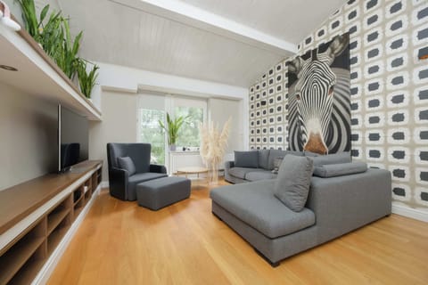 Bright and spacious living area with a comfortable sofa, stylish feature wall, and large windows overlooking the greenery.