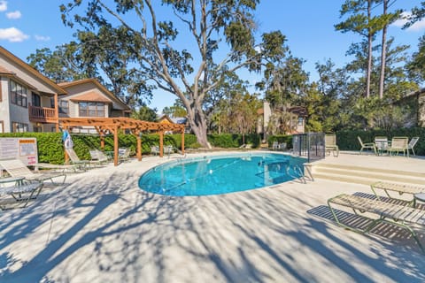 A sparkling pool nestled beneath towering oaks and Spanish moss offers a private retreat. Lounge chairs and a pergola provide shaded relaxation in this peaceful, tree-lined setting.