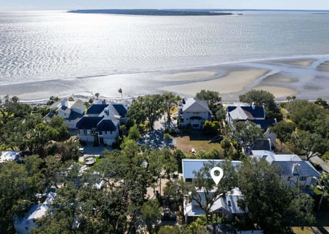 Aerial view of a coastal neighborhood situated along pristine waterfront, with homes nestled among mature trees and direct access to tidal flats and ocean views.