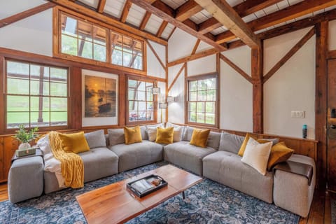 Sun-filled great room with a large sectional, soaring timber beams and wall-to-wall woodland views