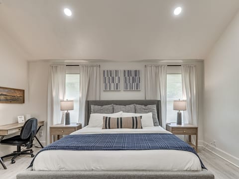 Master bedroom including a king size bed, study desk, and lounging chair. 