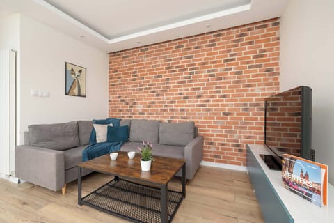 Bright and welcoming living room featuring comfortable sofa, stylish coffee table, Smart TV, and elegant exposed brick walls that add character to the space.