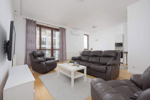Bright and spacious living room with comfortable leather sofas, a coffee table, a TV, and large windows providing plenty of natural light.