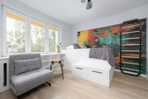 Bright and cozy studio featuring a single bed, a comfortable single sofa bed, a dining area, large windows, and colorful artwork.