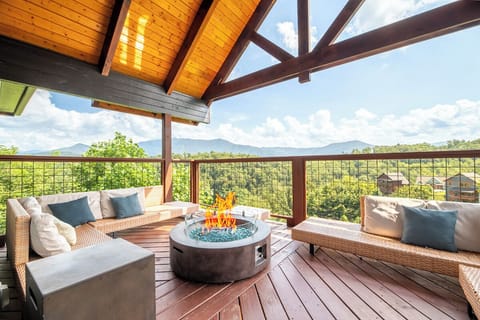 Wrap yourself in mountain serenity on this stunning covered deck, where your private fire table glows beneath soaring beams while lush forest and layered peaks stretch endlessly before you.