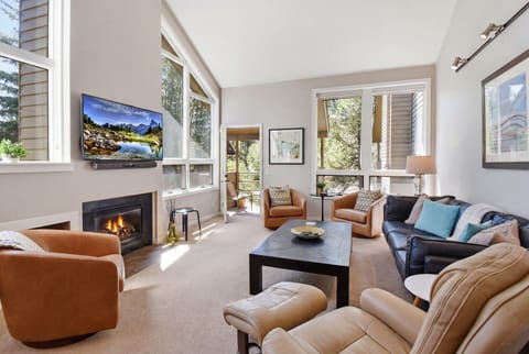 Sink into plush seating by your crackling fireplace, surrounded by sunlit windows framing serene forest views. This airy living room invites you to unwind with all the comforts of home.