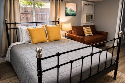 Bright, cozy bedroom with a comfortable bed, modern furnishings, natural light, blackout curtains, a leather loveseat, and warm décor—perfect for relaxing after a day of exploring.
