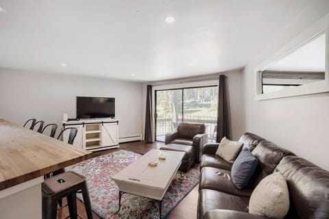 Unwind in your spacious living room with rich leather seating, a smart TV for entertainment, and a private balcony framing peaceful wooded views—perfect for relaxing mountain getaways.
