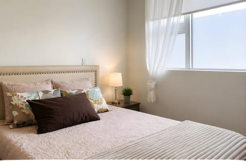 Welcome to your serene bedroom suite featuring a queen bed with a beige studded headboard and bright window lighting!