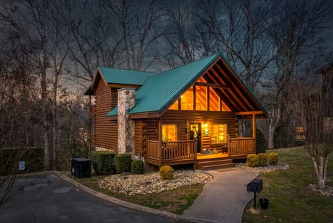 Cozy log cabin with glowing windows, covered porch, and peaceful wooded setting
