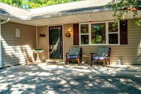 Front porch with tan siding, two cushioned wooden chairs, glass door, and a stone planter.