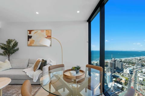 Contemporary open-plan living and dining area featuring a king sofa bed, Smart TV and floor-to-ceiling windows with sweeping southwest coastal and hinterland views.