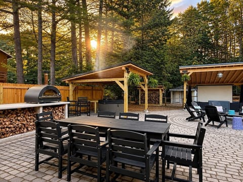 Spacious outdoor dining area with pergolas, pizza oven, hot tub, and plenty of room to gather.