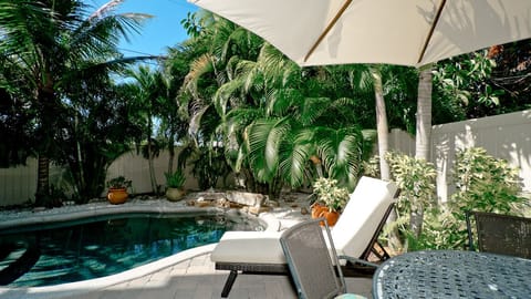 Private tropical pool oasis with loungers, shade umbrella, and lush palms
