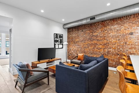 Modern open-concept living area featuring a plush dark sofa, wooden coffee table, and flat-screen TV setup.
