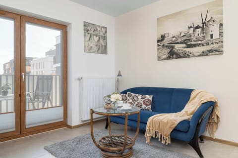 A bright living room with a sofa, armchair, and coffee table. Large balcony doors provide plenty of natural light.