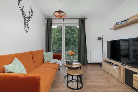 A modern living room features a  sofa placed opposite a wooden media console. Large glass doors leading to a balcony allow natural light to fill the space, creating a bright atmosphere.