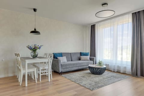 Apartament oferuje jasny salon z rozkładaną sofą, telewizorem, klimatyzacją oraz częścią jadalnianą. Duże przeszklenia prowadzą na przestronny balkon z meblami wypoczynkowymi i widokiem na okolicę.