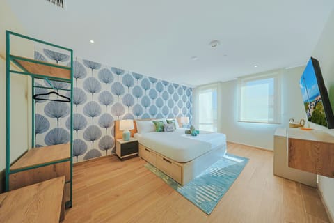 Relax in this bright, modern bedroom with stylish botanical accents, warm wood floors, and a sunny sleeping space designed for your comfort.