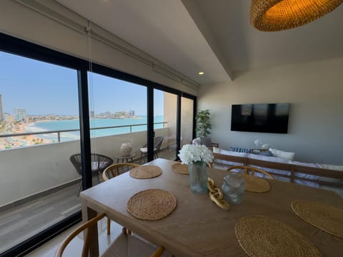 Sunlight brightens the natural wood dining table with woven placemats beside sliding glass doors to the balcony.