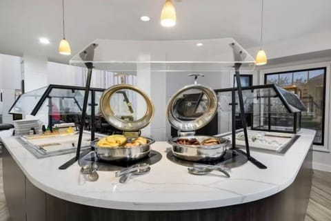 Breakfast buffet station with chafing dishes of fresh fruit and breakfast meats under glass covers
