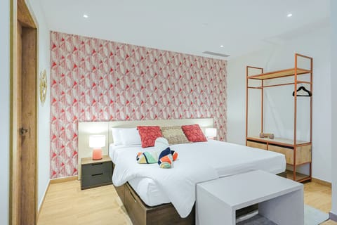 Step into your bright, cheerfully styled bedroom with crisp linens, bold accent wallpaper, and a distinctive open wardrobe—an inviting retreat for your peaceful stay.