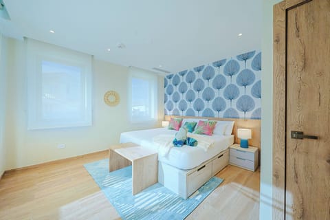 Settle into crisp white linens beneath a striking blue leaf-patterned accent wall. Natural light floods in through wide windows, while built-in storage and a cozy bench create your perfect retreat.