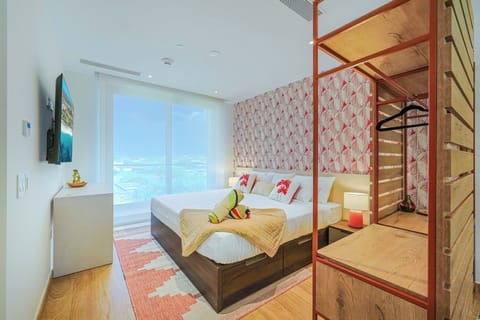 Wake up in a bright and inviting bedroom featuring floor-to-ceiling windows that fill the space with natural light. Sink into the comfortable bed surrounded by modern décor and tropical accents, creating a relaxing retreat after a day of exploring Aruba.