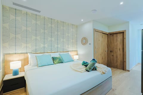Your serene coastal-inspired bedroom features a soft palette of blue and natural wood, with plush bedding, tropical accents, and thoughtful towel arrangements welcoming you to unwind in style.