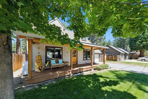 Welcome to Bear-Ski Cabin nestled in a quiet residential neighborhood, featuring a welcoming covered porch framed by mature shade trees and a lush green lawn.