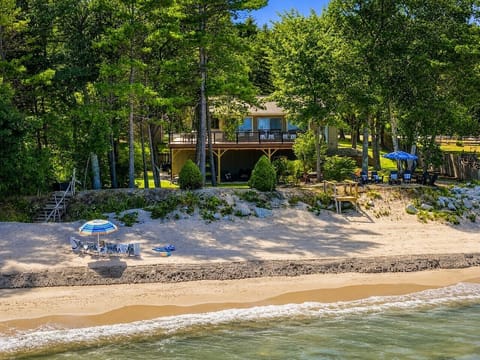 Drift + Dune sits directly on Lake Michigan, with a sandy shoreline, lakefront gathering areas, and the home tucked into a wooded setting.