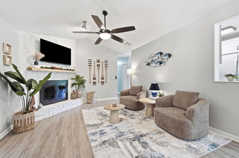 A bright coastal-inspired living room with comfortable seating, a large TV, and a statement fireplace.