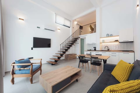 Bright and welcoming open-plan living space with modern décor, comfortable seating, a fully equipped kitchen, and a stylish loft staircase