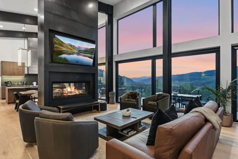 A modern living space with high ceilings, fireplace, perfect view of mountains, access to balcony and Smart TV