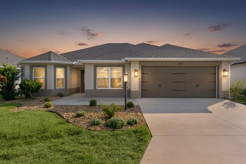 Modern single-story home with landscaped front yard and spacious driveway, set in a peaceful residential neighborhood at sunset.