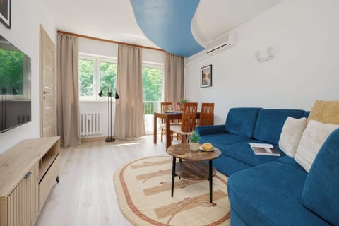 A bright living room with a comfortable sofa bed and a dining area. Large balcony doors let in plenty of natural light.