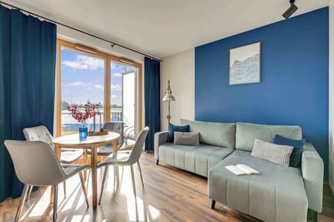 Jasny i przestronny salon z dużymi przeszkleniami, które zapewniają dostęp do naturalnego światła i otwierają wnętrze na widok. Wygodna sofa, elegancka jadalnia oraz harmonijna aranżacja tworzą komfortową przestrzeń do wypoczynku i wspólnego spędzani