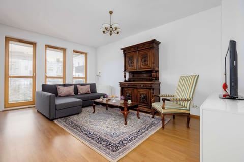 A spacious living room features a comfortable sofa resting. A large, ornate wooden cabinet stands prominently against the wall, alongside a classic armchair and large windows.