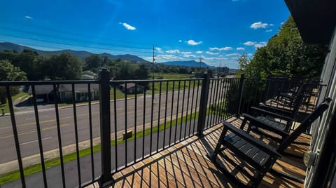 Balcony seating overlooks a quiet neighborhood with mountain views framing the horizon beyond the tree-lined street.