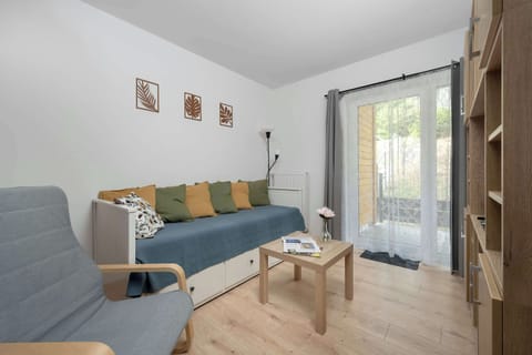 A cozy living room features a comfortable sofa adorned with pillows. A small wooden coffee table sits on the light wooden floor, with a glass door leading to a terrace.